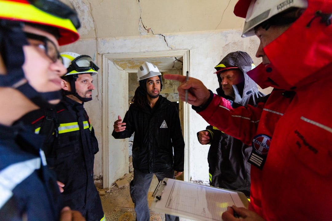 3 Homens Em Jaqueta Vermelha E Preta De Pe Ao Lado Da Parede Branca Durante O Dia 0LnH9j9Wirw