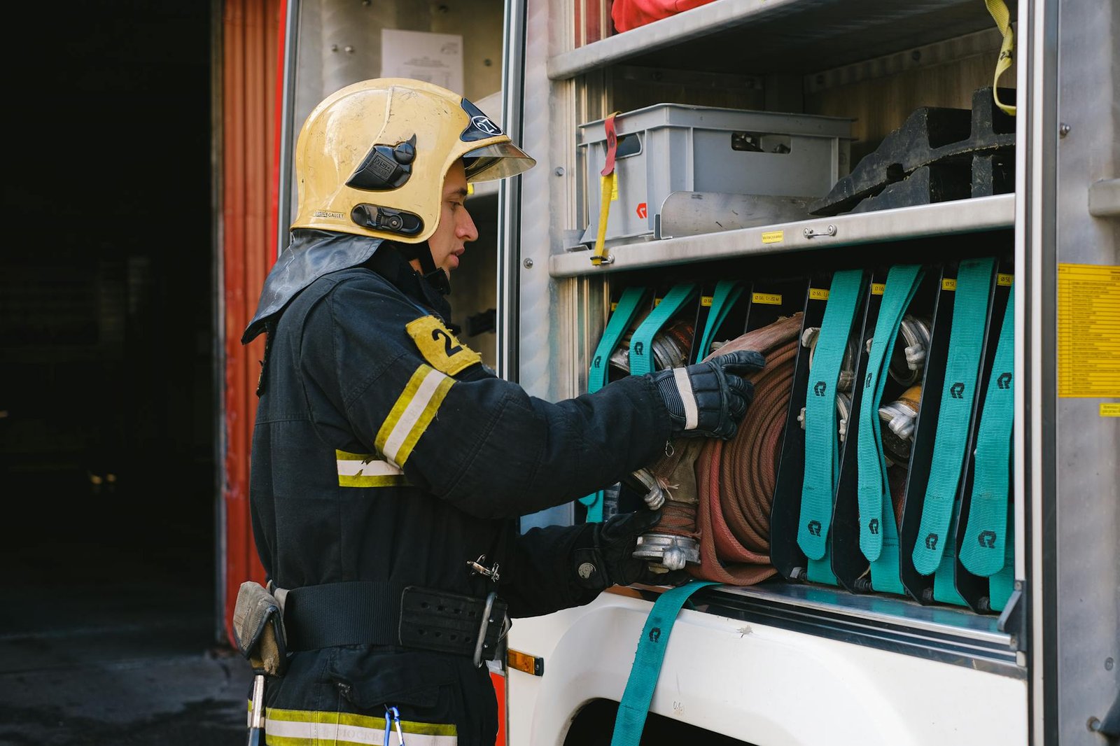 A firefighter in full gear organizes hoses in a fire truck, demonstrating safety and preparedness.