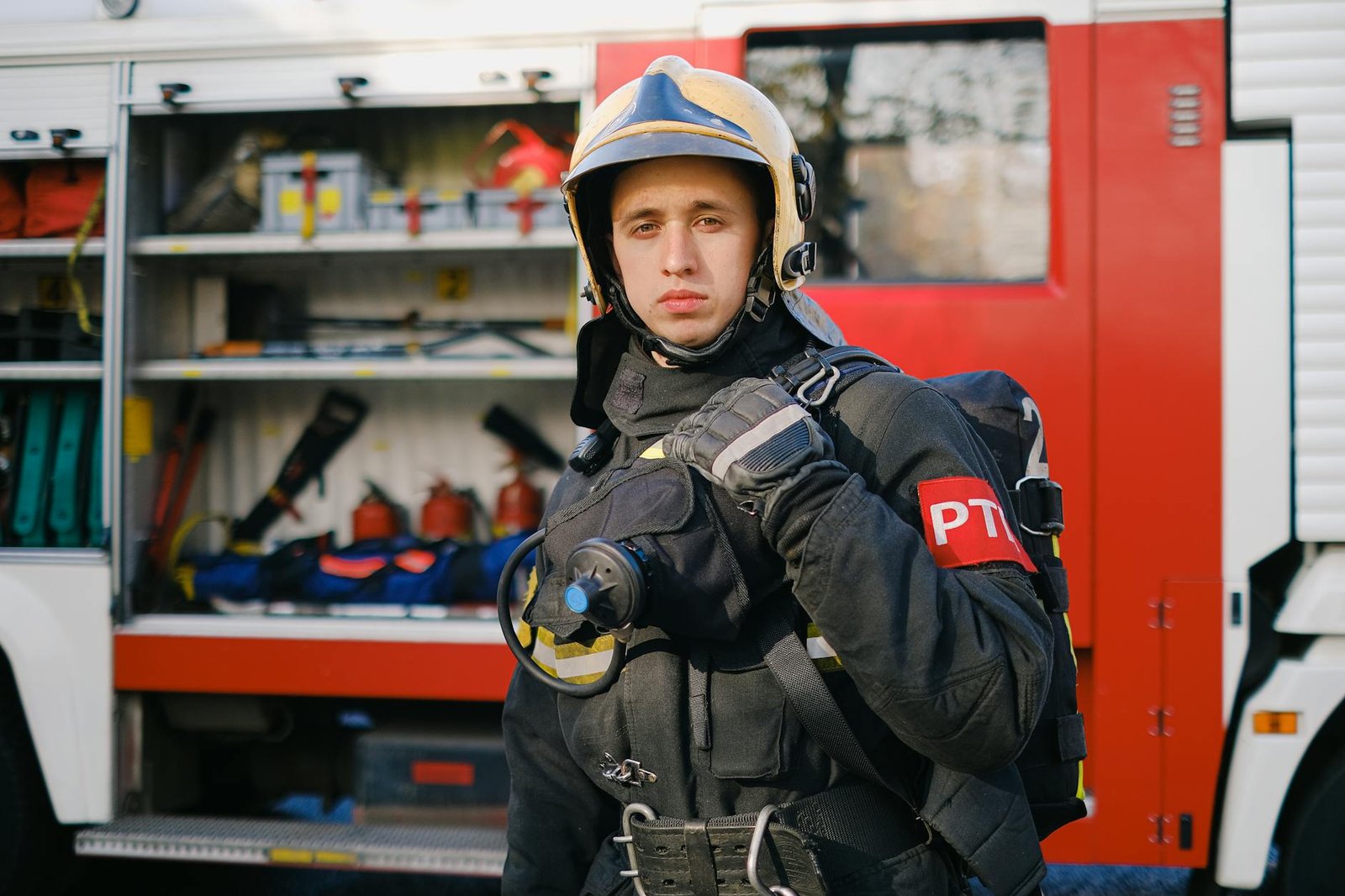 A firefighter in uniform stands confidently next to a fire truck, showcasing readiness.