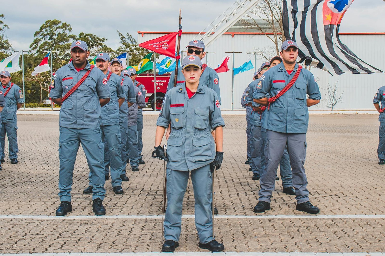 Uniformed soldiers standing in formation outdoors with flags displayed in the background.