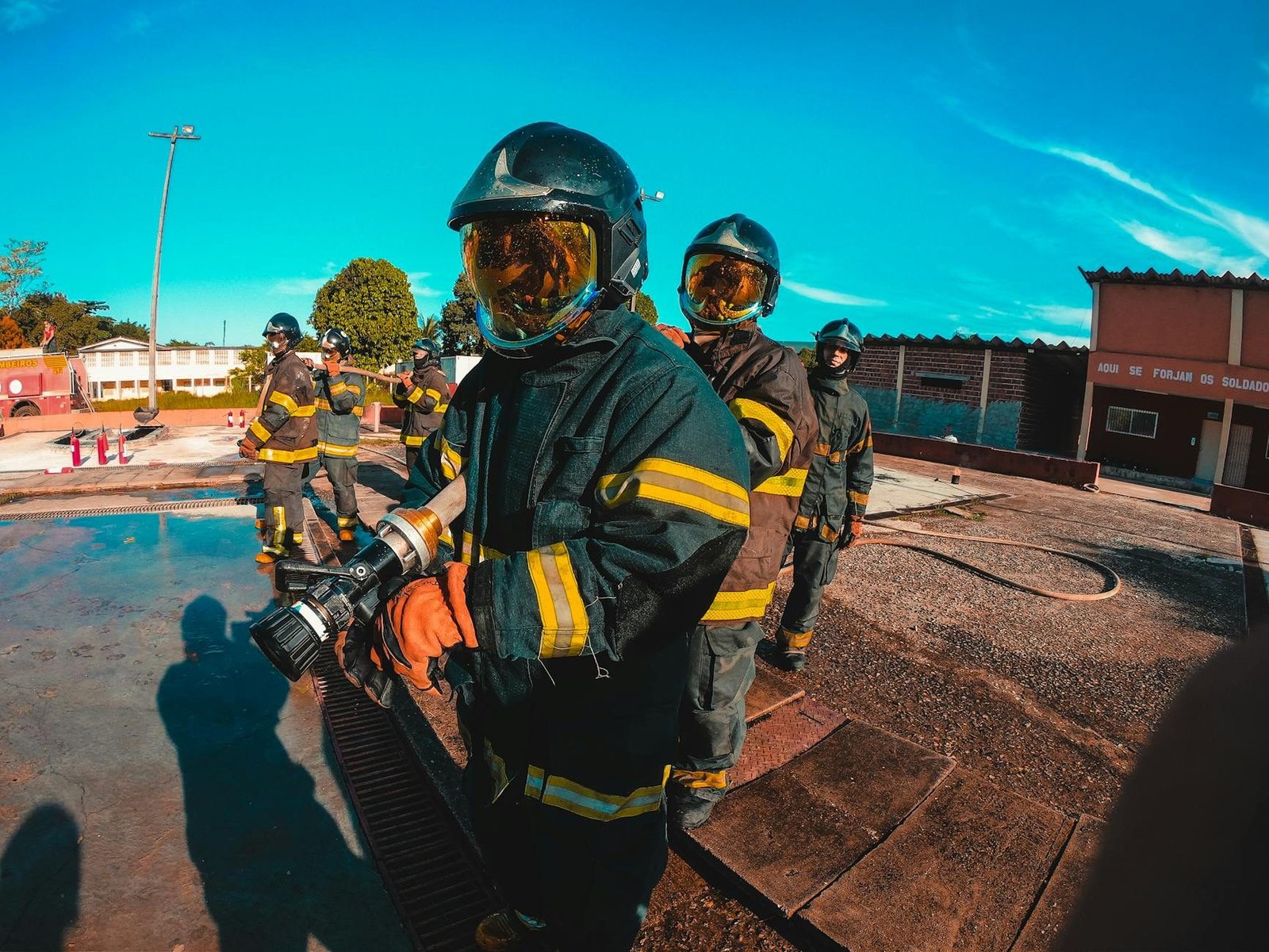 Firefighters in protective suits and helmets manage equipment during training outdoors.