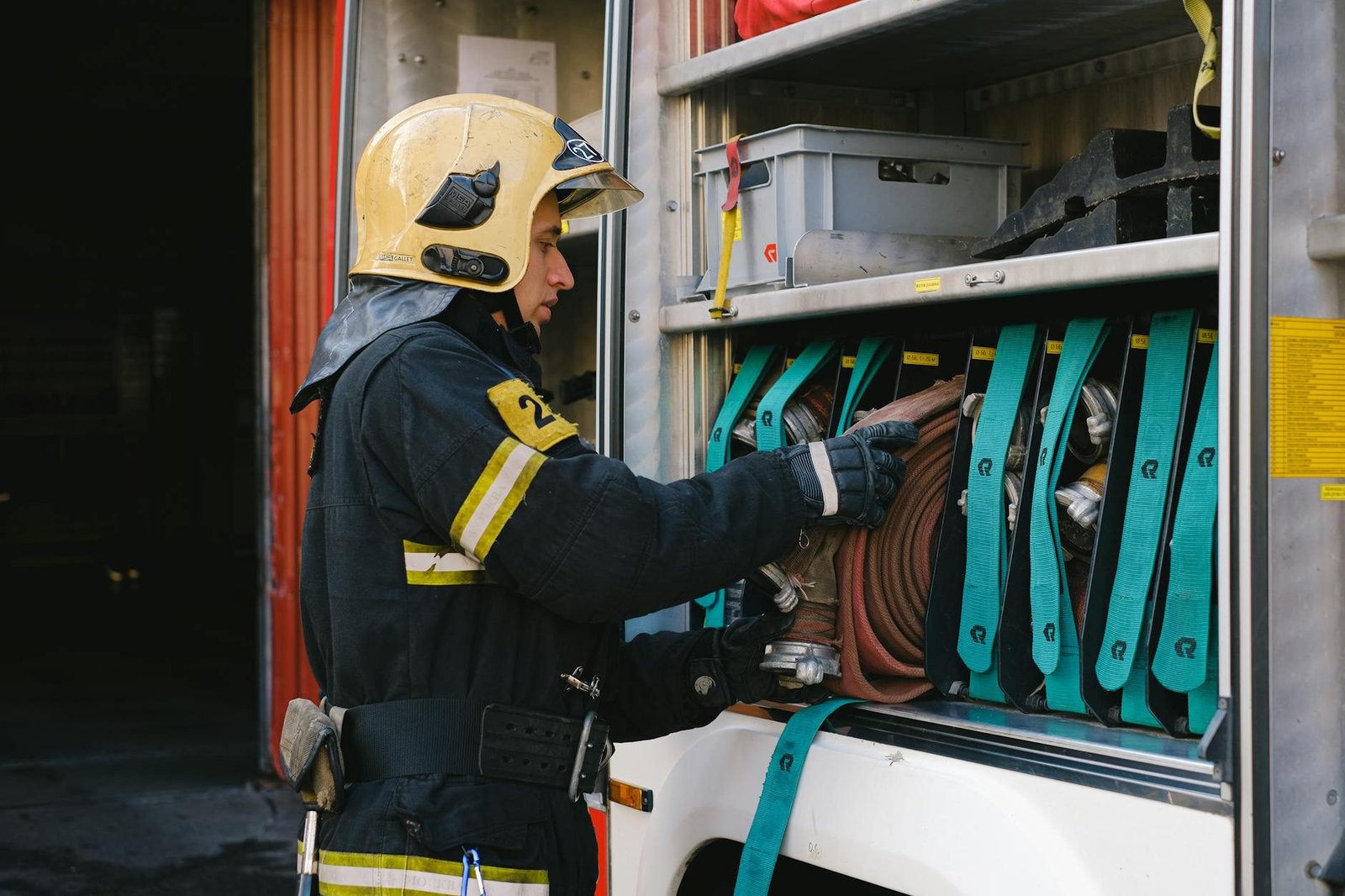 A firefighter in full gear organizes hoses in a fire truck, demonstrating safety and preparedness.