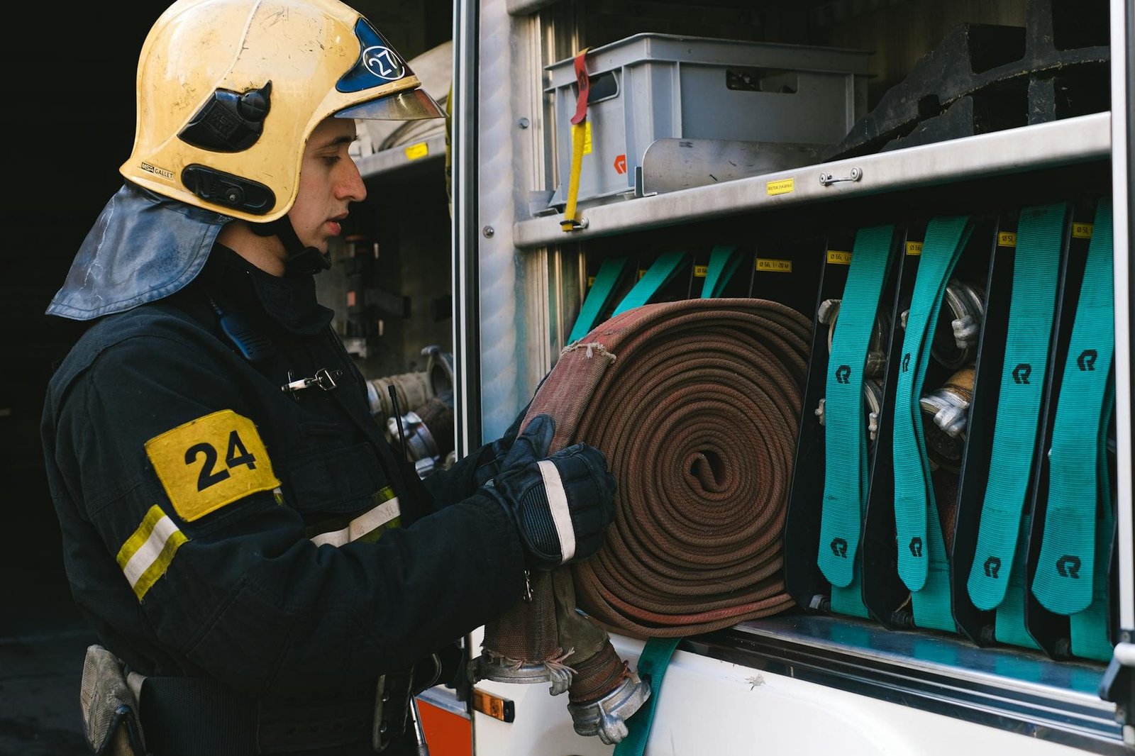 Firefighter organizing hoses in a fire truck, focusing on readiness and safety.